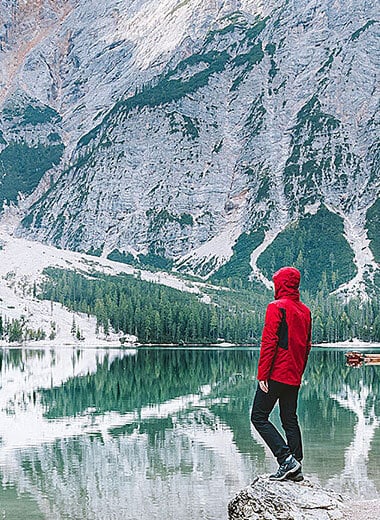 person standing next to high alpine lake with snowy mountains